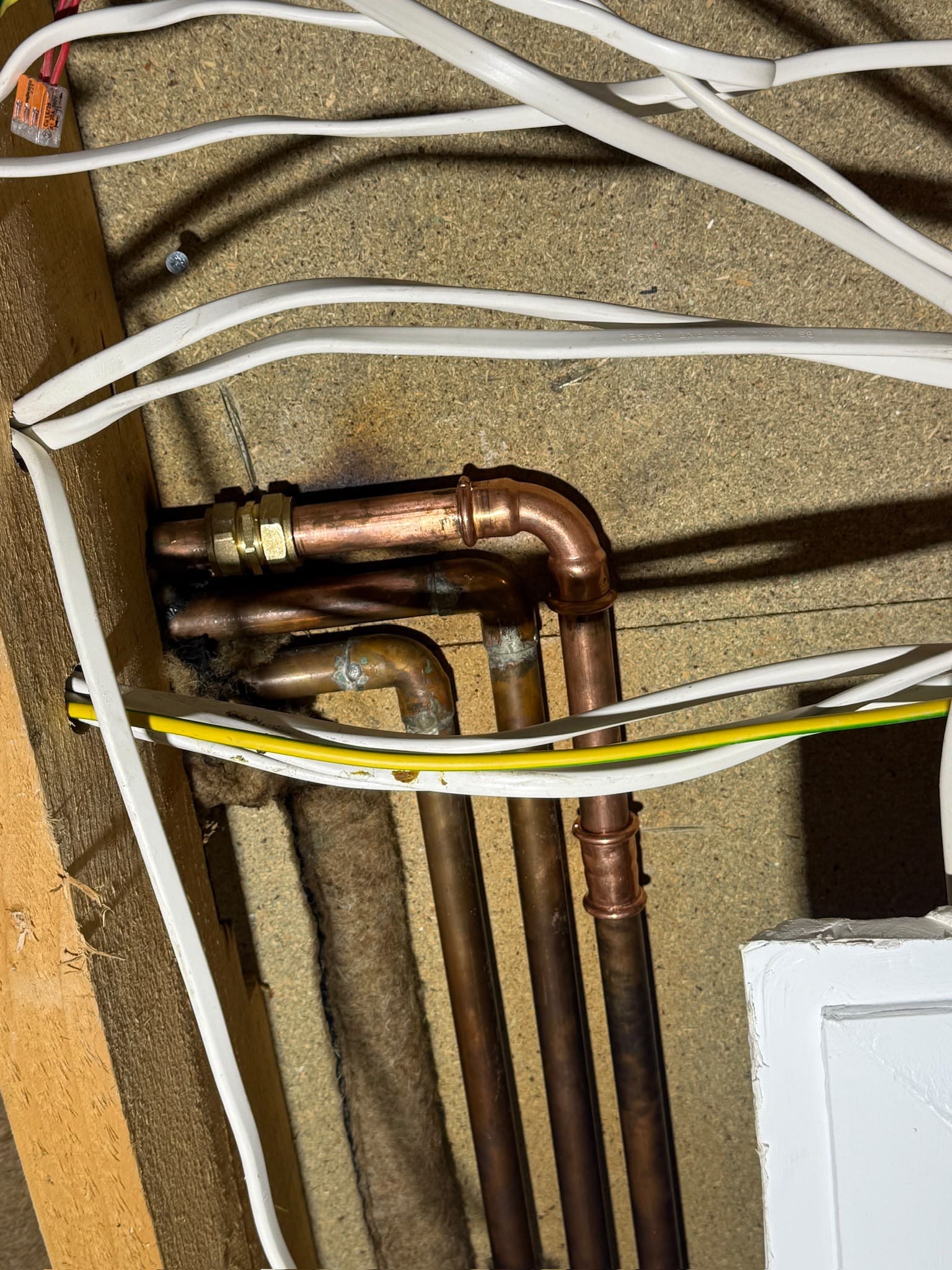 Copper pipework with soldered joints and electrical cabling exposed inside a wall or ceiling cavity during plumbing/electrical work.